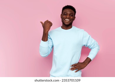 african american man in blue sweater smiles and shows his hand to the side on pink isolated background, man advertises copy space - Shutterstock ID 2353701109