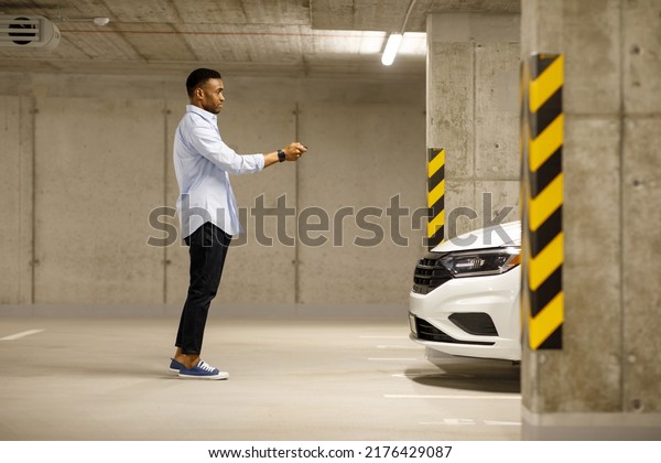 African american man with car keys in front of\
car in underground\
parking.