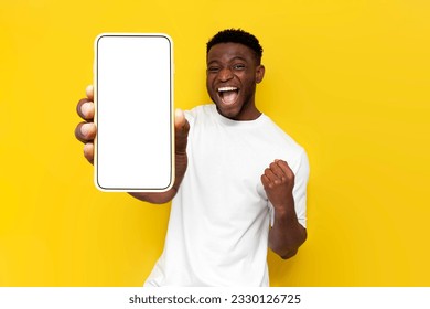 african american man celebrating victory and showing blank screen of smartphone on yellow isolated background, winner guy rejoices in success and luck and advertises copy space on phone display - Powered by Shutterstock