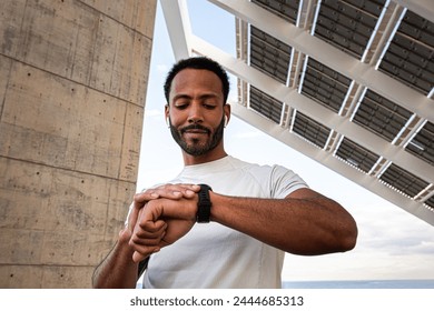 African American man checking pulse in smart watch. Black male athlete with wireless earphones using smart watch to put on music. Sport and technology concept.