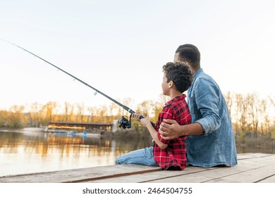 African American man and child sitting on a wooden pier holding fishing rods on the river, dad teaching his son to fish in the lake, family resting and relaxing on the weekend - Powered by Shutterstock