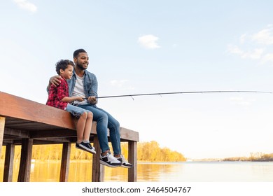 African American man and child sitting on a wooden pier holding fishing rods on the river, dad teaching his son to fish in the lake, family resting and relaxing on the weekend - Powered by Shutterstock