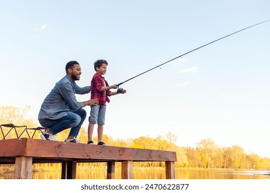 African American man and child sitting on a wooden pier holding fishing rods on the river, dad teaching his son to fish in the lake, family resting and relaxing on the weekend - Powered by Shutterstock