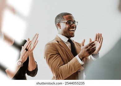 African American man clapping, celebrating business success. The professional man is clapping, smiling in a team business meeting. People clapping in the background with sunlit overlay. - Powered by Shutterstock