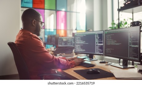 African American Man Coding On Desktop Computer With Professional Multiple Monitors Setup In Creative Office. Male Software Engineer Developing Mobile Application For Innovative Start-Up.