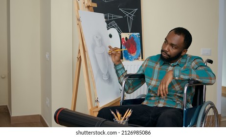 African american man and disability using pencil to draw canvas  learning new artistic skills in art class and teacher  Young student in wheelchair drawing skethc masterpiece in workshop 