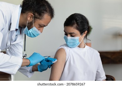 African American Man Doctor Wearing Protective Medical Mask And Gloves Injecting Vaccine To Young Indian Woman Patient In Hospital, Holding Syringe, Vaccination And Healthcare, Coronavirus Concept