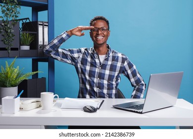 African american man doing military soldier salute while looking at camera in office workspace. Young adult person doing patriotic greeting with honor and respect for veterans servicemen.