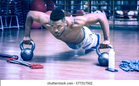 African american man doing push up workout in dark gym using kettlebell - Black gritty face guy working on chest muscles exercise at fitness center - Bluish vintage filter look with dim light effect - Powered by Shutterstock