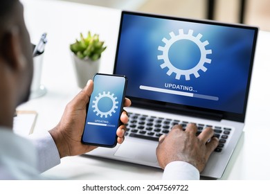 African American Man Doing Software Update On Mobile Phone And Laptop