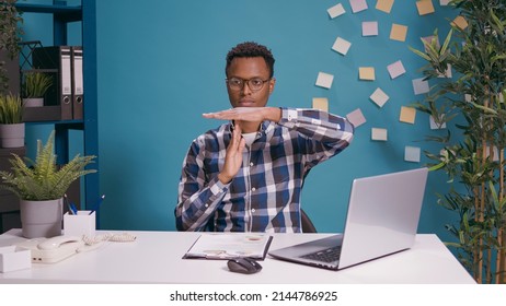 African american man doing t shape sign with hands, showing timeout gesture in front of camera. Person working on laptop computer and advertising symbol to take break from overtime work.