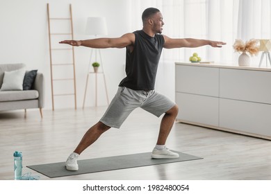 African American Man Doing Yoga Standing In Warrior Pose At Home. Black Guy Practicing Relaxing Exercises Training In Living Room Indoors. Virabhadrasana Asana. Side View Shot - Powered by Shutterstock