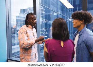 African American man explaining ideas to Asian woman and biracial man in a modern business office. They are standing in front of a glass wall with notes, unaltered. - Powered by Shutterstock