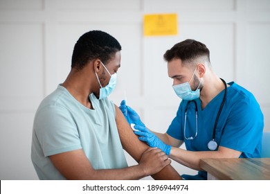 African American Man In Face Mask Receiving Coronavirus Immunization, Taking Shot Of Covid-19 Vaccine At Medical Office. Health Care, Treatment And Prevention Of Viral Diseases Concept