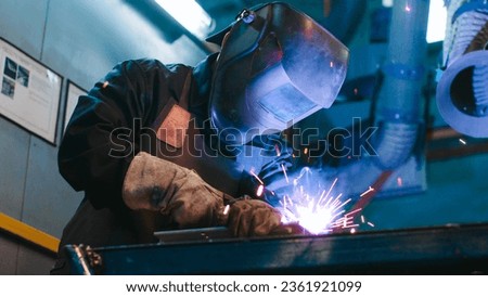 African American man is focused on work. Uniformed welder lifts protective mask and look straight at camera. Male is happy and smiles. Men's labor. Diversity of men's profession.