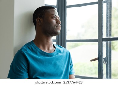 African American man gazing out window, reflecting peacefully at home. Contemplation, tranquility, lifestyle, relaxation, solitude, reflection - Powered by Shutterstock