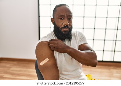African American Man Getting Vaccine Showing Arm With Band Aid Thinking Attitude And Sober Expression Looking Self Confident 