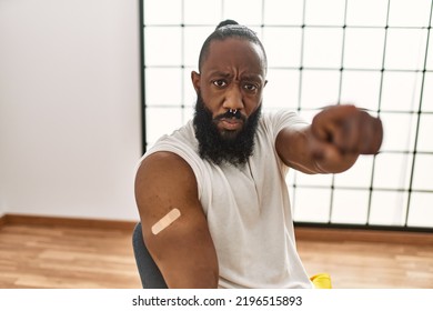 African American Man Getting Vaccine Showing Arm With Band Aid Pointing With Finger To The Camera And To You, Confident Gesture Looking Serious 