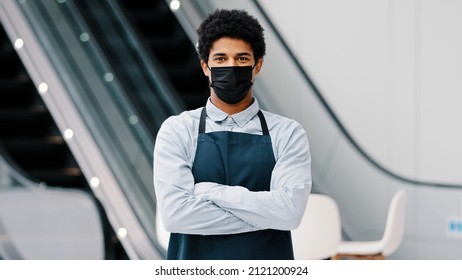 African American Man Guy Restaurant Cafe Male Worker In Medical Mask Looking Camera Posing Crossing Arms Waiter Salesman Wearing Apron Standing At Work Space Covid Pandemic Quarantine. Small Business