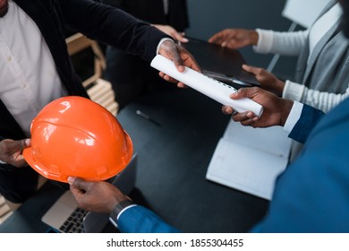 An African American man hands over a building permit and an orange construction helmet to an investor. The concept of business, construction, financing