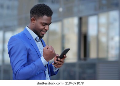 African American man happy winning tender for business after upgrading startup. Mature businessman looks for excellent results on smartphone with smile - Shutterstock ID 2194891079