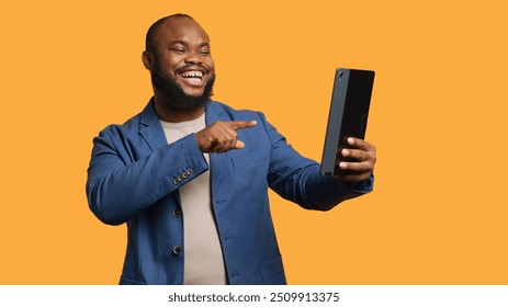 African american man having funny conversation with friends during teleconference meeting using tablet, studio background. Person laughing, having fun with mates during internet videocall, camera A - Powered by Shutterstock