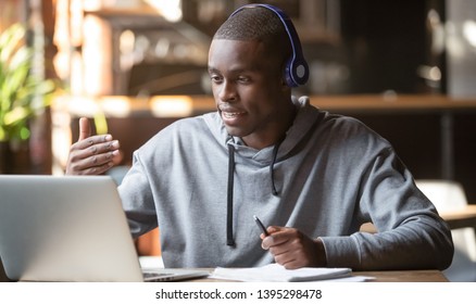 African American man in headphones making video call in cafe, using laptop, talking, watching webinar or studying language, black student speaking, making notes, online training, explaining