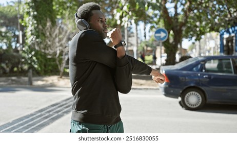 African american man with headphones stretching on urban street with cars and trees - Powered by Shutterstock