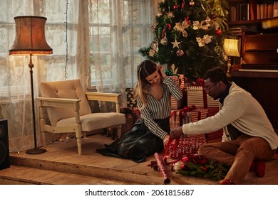 African American Man And His Caucasian Girlfriend Sitting On The Floor And Unwrapping Christmas Present