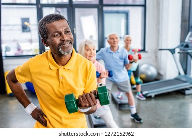 african american man and his friends synchronous exercising with dumbbells at sports hall - Powered by Shutterstock