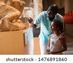 African American man and his little daughter looking at exhibits of antique sculpture at historical museum