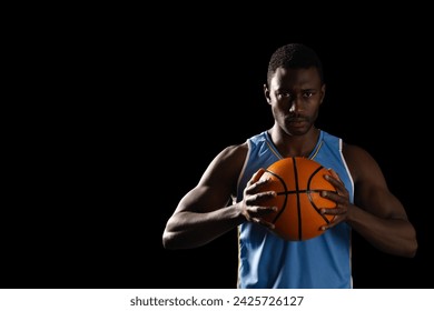African American man holding a basketball on a black background, with copy space. His focused expression and athletic stance suggest determination and skill.