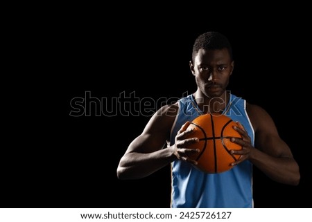 African American man holding a basketball on a black background, with copy space. His focused expression and athletic stance suggest determination and skill.