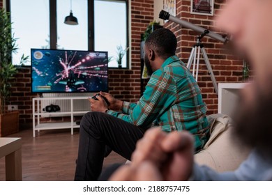 African American Man Holding Console Controller To Play Video Games With Shooting Competition. Playing Shooter Game On Television, Having Fun With Cheerful Friends At House Party.