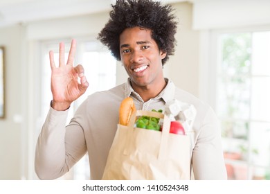 African American Man Holding Groceries Bag With Fresh Vegetables At Home Doing Ok Sign With Fingers, Excellent Symbol