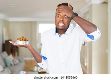 African American Man Holding Metal Bowl With Cat Or Dog Dry Food Stressed With Hand On Head, Shocked With Shame And Surprise Face, Angry And Frustrated. Fear And Upset For Mistake.