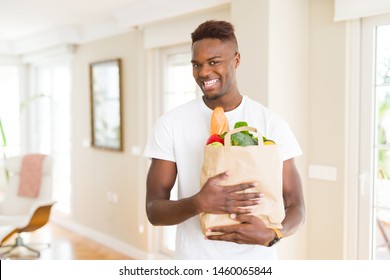 African american man holding paper bag full of groceries happy and smiling confident - Powered by Shutterstock