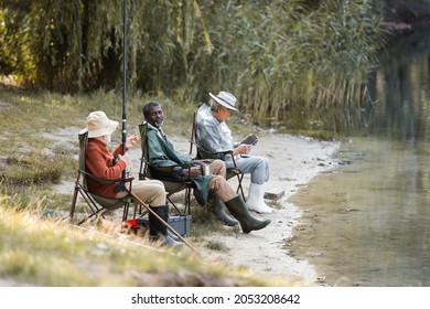 African American Man Holding Thermo Cup Near Interracial Friends Fishing Near Lake