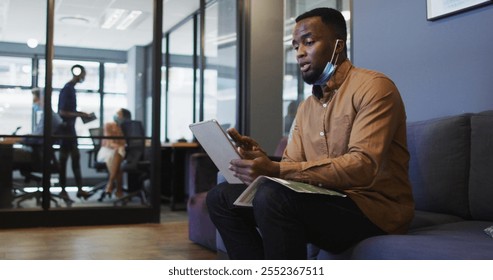 African american man with lowered face mask having image chat on digital tablet at modern office. social distancing quarantine lockdown during coronavirus pandemic - Powered by Shutterstock