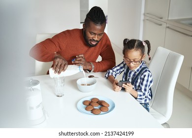 African American Man Making Breakfast For His Daughter While She Playing On The Smartphone