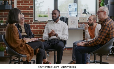 African American Man Making Confession About Addiction And Rehabilitation With People At Group Therapy. AA Meeting With Patients Talking About Alcoholism And Progress In Circle.