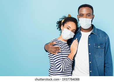 African American Man In Medical Mask Looking At Camera While Hugging Wife Isolated On Blue