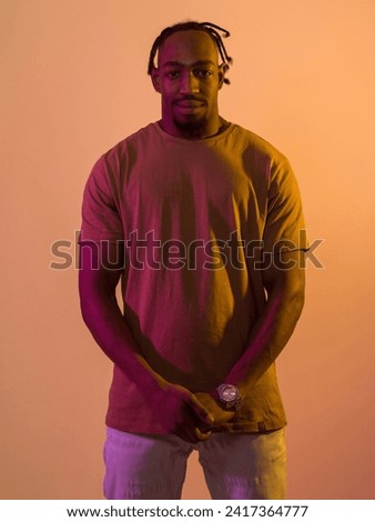 African American man with a modern and stylish haircut exudes confidence and charisma as he strikes a pose against an orange backdrop, showcasing a bold and vibrant expression of contemporary fashion