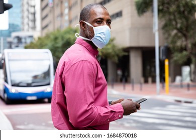 African American man out and about in the city streets during the day, wearing a face mask against air pollution and covid19 coronavirus, crossing the street and using his smartphone. - Powered by Shutterstock