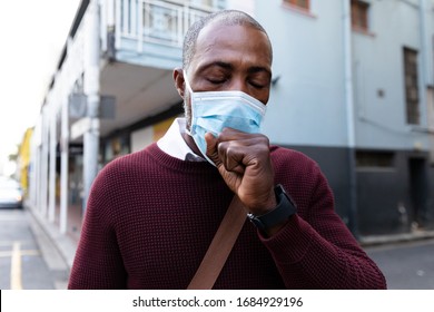 African American Man Out And About In The City Streets During The Day, Wearing A Face Mask Against Air Pollution And Covid19 Coronavirus, Covering His Face While Coughing. 