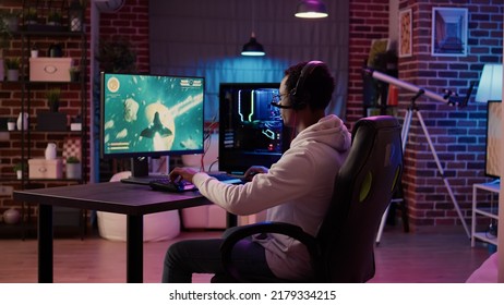 African american man playing fast paced multiplayer space shooter using pc gaming setup having a good time in home living room. Gamer streaming online simulation game while talking in headset.