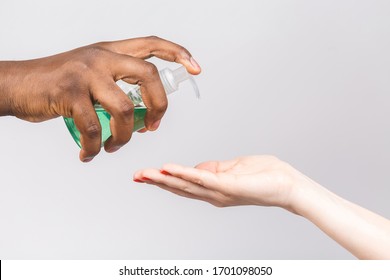 African American Man Posing Isolated On White. Epidemic Pandemic Coronavirus 2019-ncov Sars Covid-19 Flu Virus. Holding Bottle With Antibacterial Sanitizer Applying It On Woman's Hand.