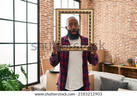 African american man putting face in empty frame in shock face, looking skeptical and sarcastic, surprised with open mouth 