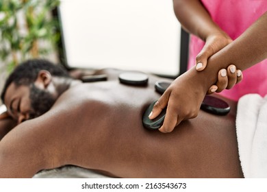 African american man reciving back massage with black stones at beauty center.