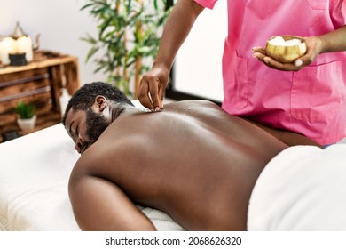 African american man reciving skin treatment on his back with mineral salts at beauty center.